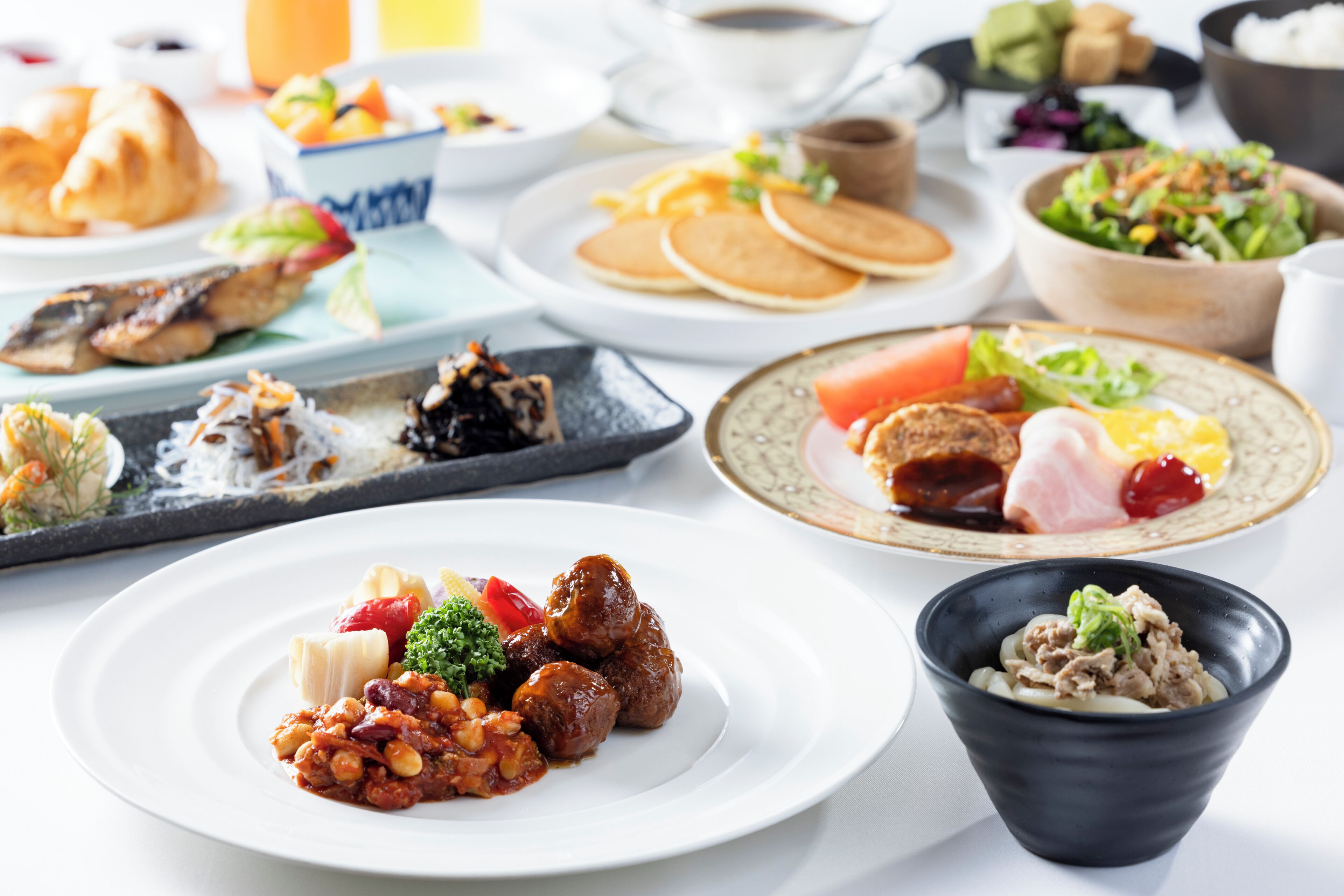 A variety of dishes on a table, including a plate with meatballs and vegetables, a bowl of salad, and several other plates with different foods.