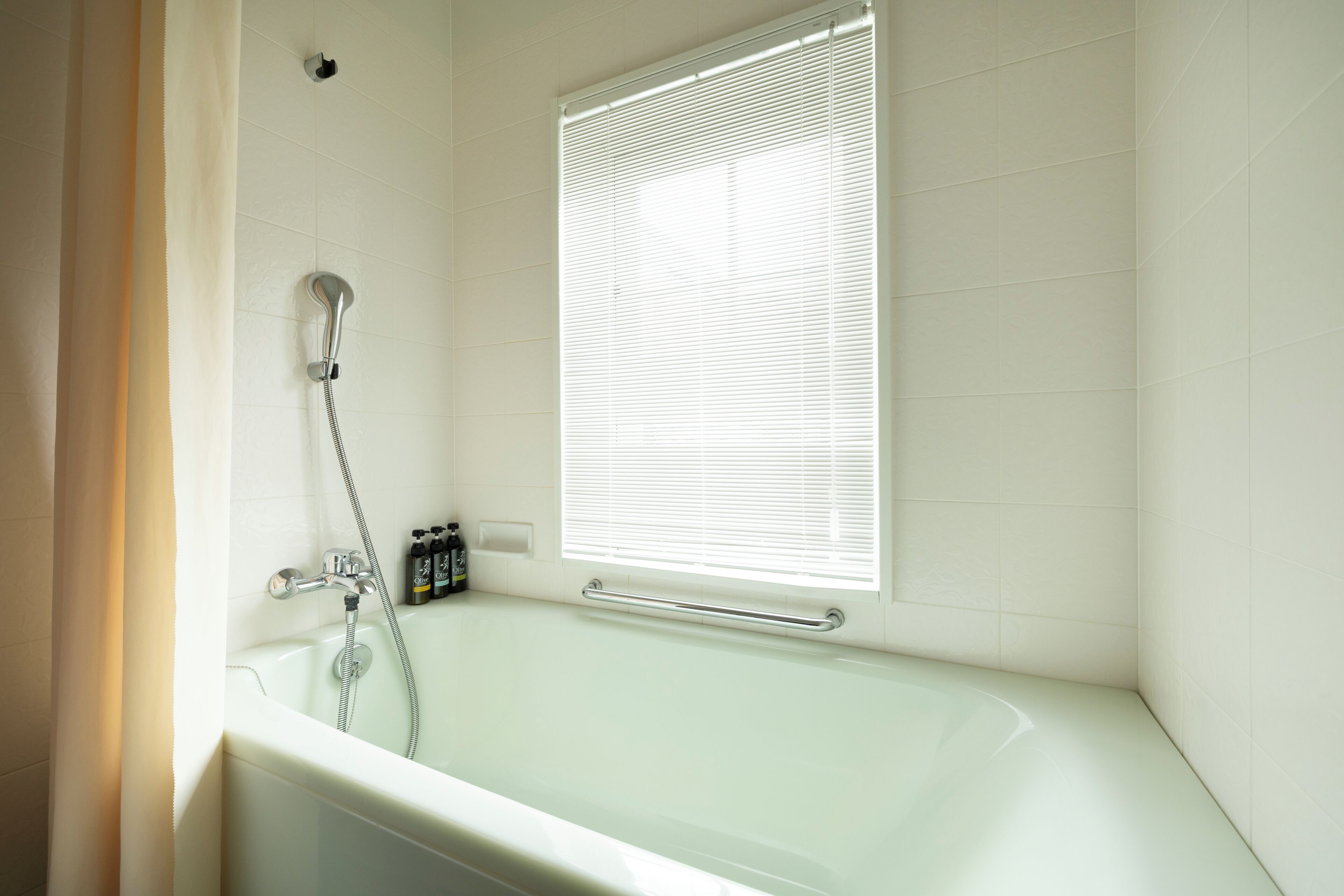Un baño con bañera, ducha y ventana con persianas.