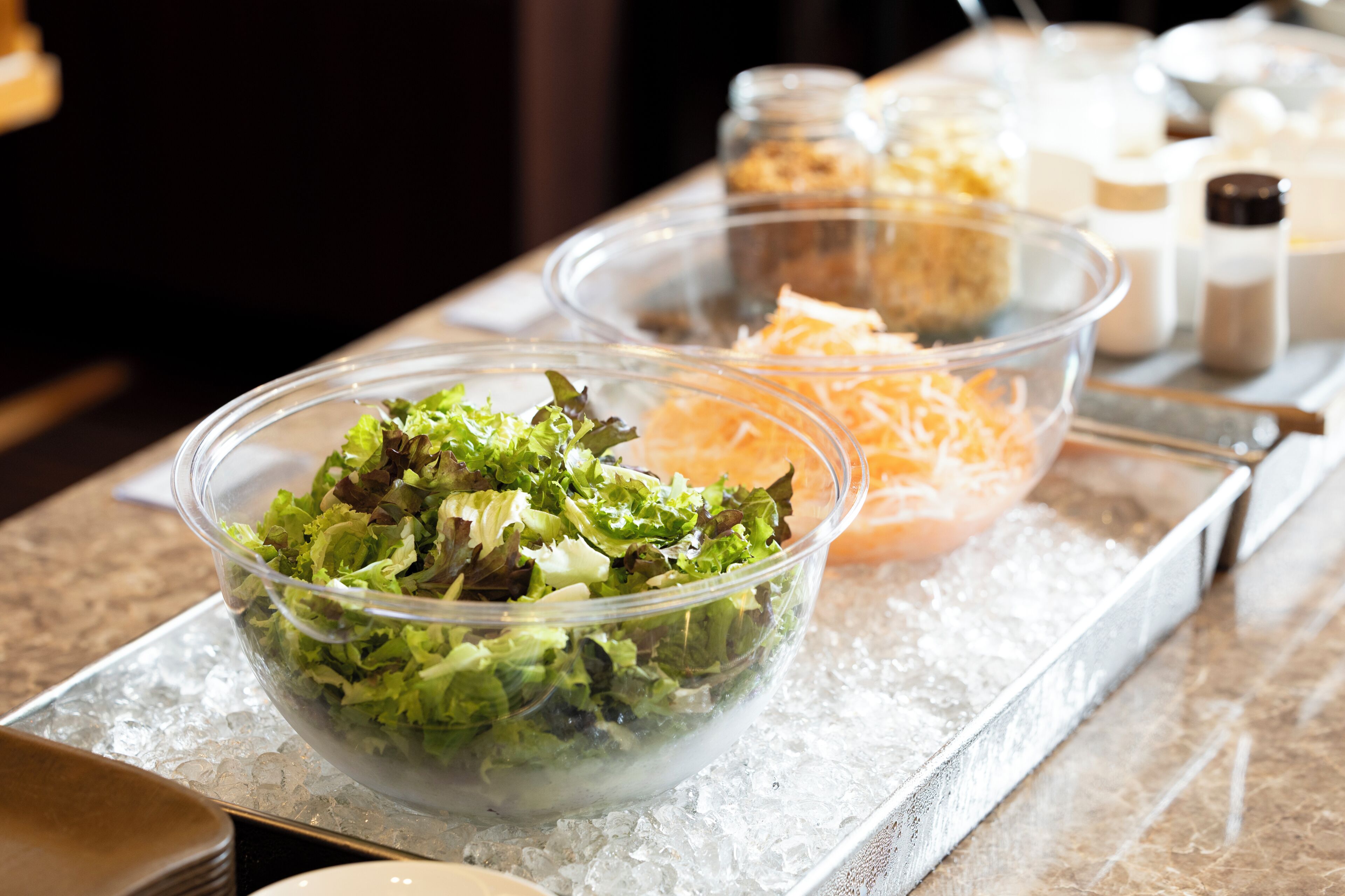 A buffet table with various food items including a bowl of salad, a container of shredded cheese, and several condiments.