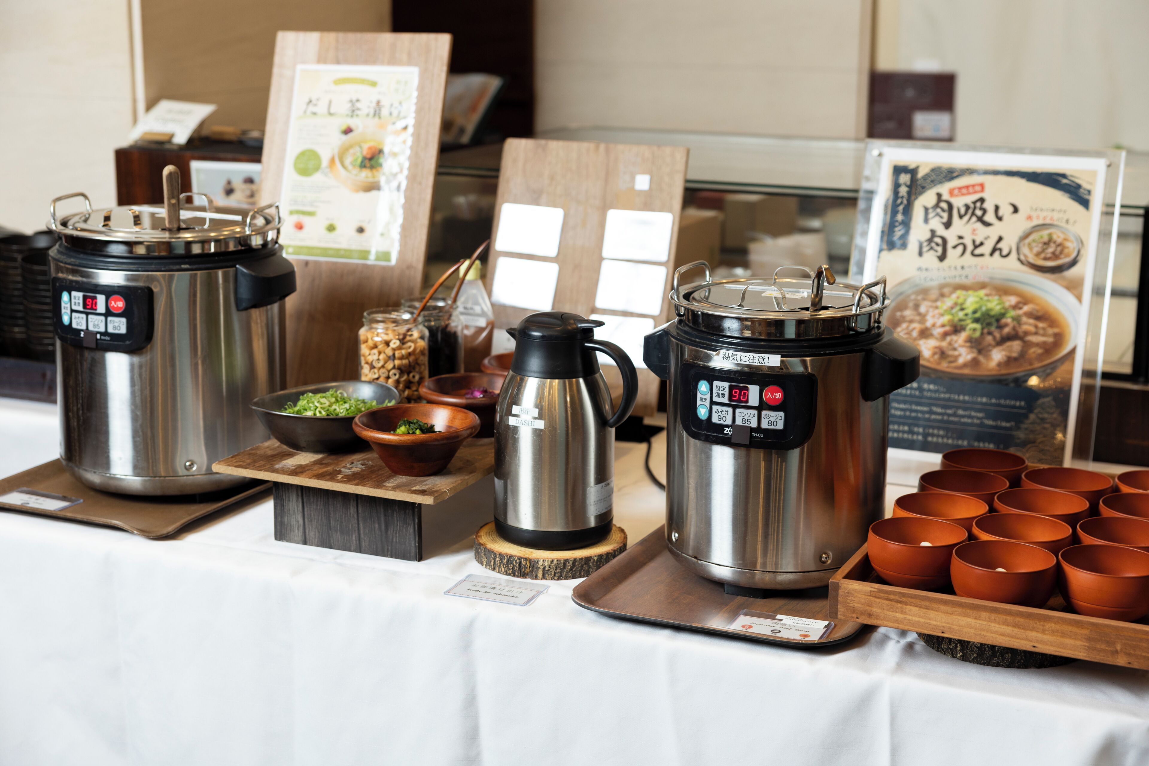 A table with two electric kettles, a coffee pot, and a tray of cups.
