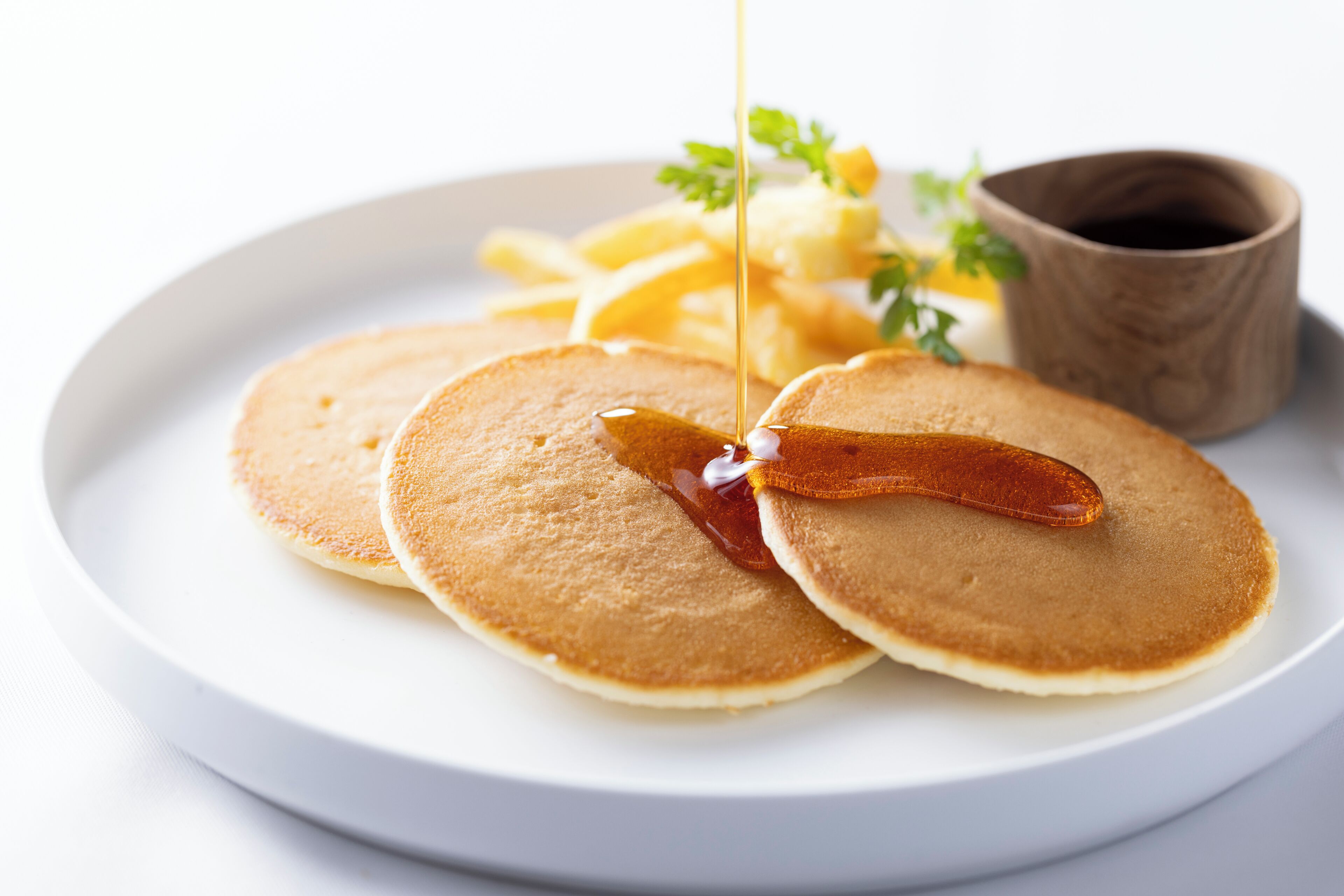 A plate with pancakes and syrup, a wooden cup, and a small bowl of fruit.