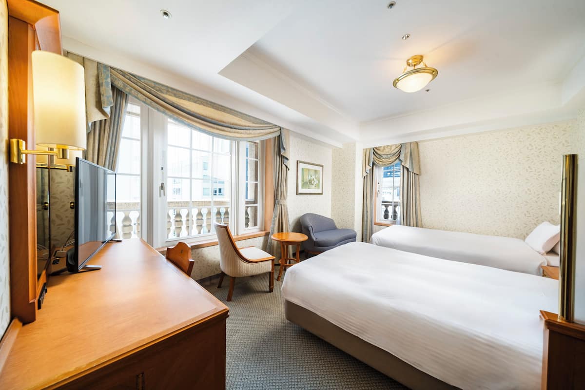 Une chambre d’hôtel avec deux lits, un bureau, une chaise, une télévision et une fenêtre avec des rideaux.