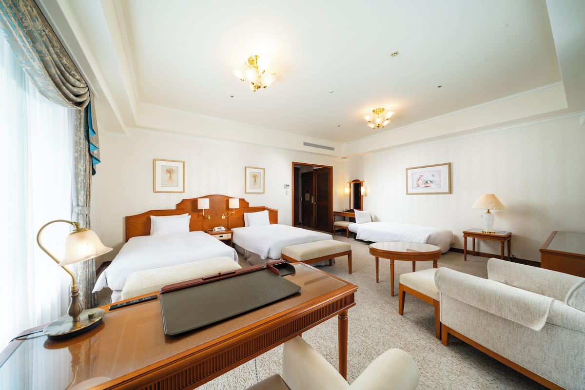 Une chambre d’hôtel avec deux lits, un bureau, une chaise, un canapé et une petite table.