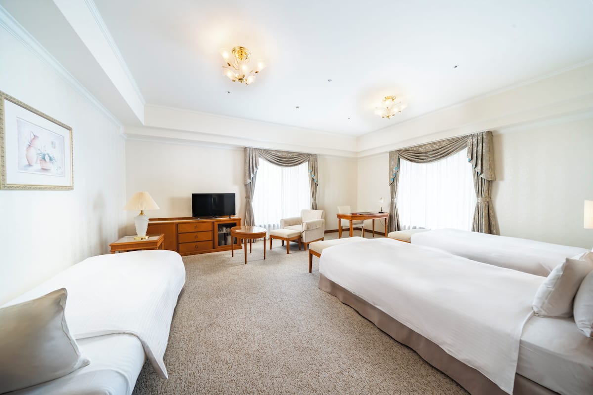 Une chambre d’hôtel avec deux lits, un bureau, une chaise, une télévision et une lampe.