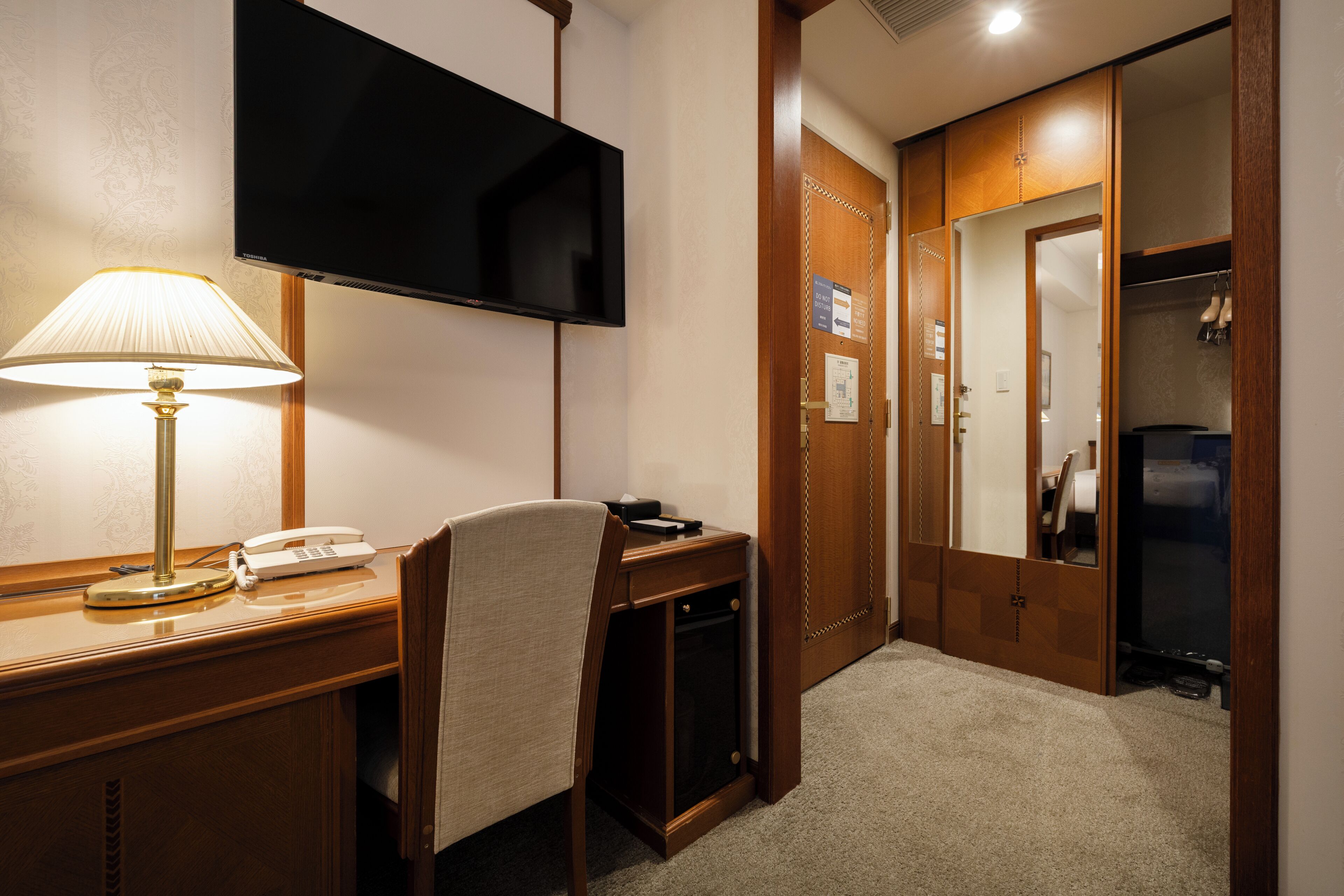 Habitación de hotel con escritorio, teléfono, televisión fijada en la pared y una puerta que da a un armario.
