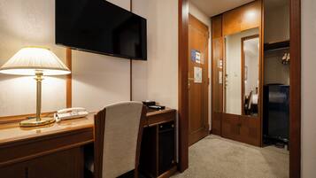 Habitación de hotel con escritorio, teléfono, televisión fijada en la pared y una puerta que da a un armario.