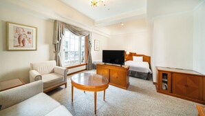 Ein Hotelzimmer mit einer Couch, einem Glastisch, einem Fernseher, einem Holzschrank und einem Bett.