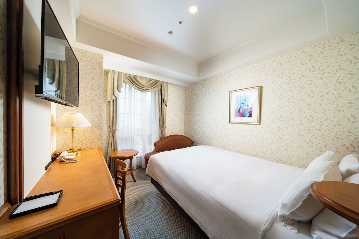 Une chambre d’hôtel avec un lit, un bureau doté d’une lampe, une chaise et une petite table.