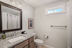 Une salle de bain avec un lavabo à vasque en granit, des toilettes blanches, un tableau encadré au mur et une fenêtre située au-dessus des toilettes.