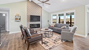 A living room with a fireplace, a ceiling fan, and a large window offering a view of the outdoors. - New Home in west Manhattan,  Family Friendly and close to KSU! (Manhattan)