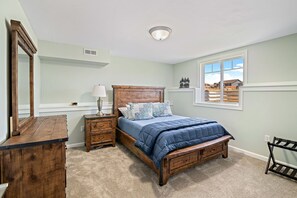Une chambre à coucher avec un lit en bois, une commode, une table de chevet, une lampe et une fenêtre donnant sur des maisons.