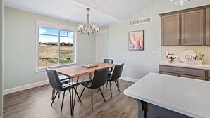 A modern kitchen with a large island, a dining area with a table and chairs, and a view of a field through the window. - New Home in west Manhattan,  Family Friendly and close to KSU! (Manhattan)