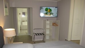 Quarto de hotel com cama, luminária, guarda-roupa, cabideiro e televisão na parede.