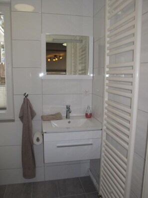 Un baño con un lavabo blanco, espejo, toallero y una toalla colgada.
