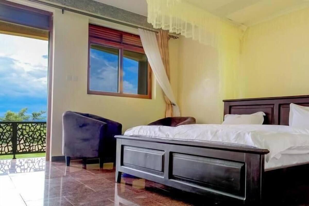 A bedroom with a bed, a chair, a window with curtains, and a balcony.