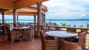 A covered outdoor seating area with wicker furniture and a view of the sea.