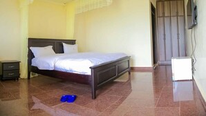 A bedroom with a bed, a nightstand, a wardrobe, and a television. - Fancy Resort Beach Hotel (Jinja)