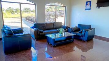 Una sala de estar moderna con un gran ventanal que da a un área exterior, un juego de sofá azul y una mesa de centro de vidrio.