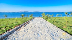 A pathway leading to a beach with a clear view of the sea and distant hills. - Fancy Resort Beach Hotel (Jinja)