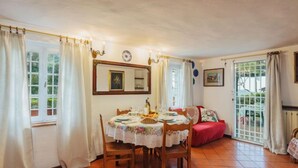 Ein Essbereich mit einem Tisch, der für vier Personen gedeckt ist, umgeben von Stühlen, einem roten Sofa und einem großen Fenster mit Vorhängen.