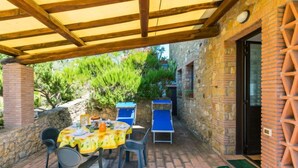 An outdoor patio with a covered area, stone walls, and a table set for dining. - Libeccio by Interhome (Marina di Bibbona)