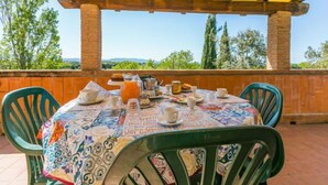 Une terrasse extérieure avec une table dressée pour le petit-déjeuner, entourée de murs en briques et d’une pergola jaune.