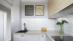 A modern kitchen with a black sink, white cabinets, a wooden countertop, and a vase with flowers. - Elite Apartments Przymorze (Gdansk)