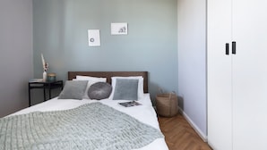 A bedroom with a bed, pillows, a blanket, a nightstand, a lamp, and a wardrobe. - Elite Apartments Przymorze (Gdansk)