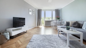 A modern living room with a flat-screen TV, white furniture, a grey sofa, and a view of the outdoors through large windows. - Elite Apartments Przymorze (Gdansk)