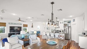A modern kitchen with white cabinets, stainless steel appliances, and a dining area with a wooden table and chairs. - The Blue Pearl- Gulf view home, Short stroll to beach, Community pool, Sleeps 10 (Port St. Joe)