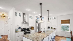 A modern kitchen with white cabinetry, stainless steel appliances, and a granite island with bar stools. - The Blue Pearl- Gulf view home, Short stroll to beach, Community pool, Sleeps 10 (Port St. Joe)