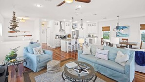 A spacious living room with a ceiling fan, light-colored sofas, a coffee table, and a dining area with a view. - The Blue Pearl- Gulf view home, Short stroll to beach, Community pool, Sleeps 10 (Port St. Joe)