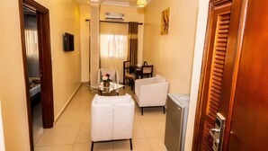 Habitación de hotel con cama, escritorio, dos sillas, mesa con un jarrón y televisor.