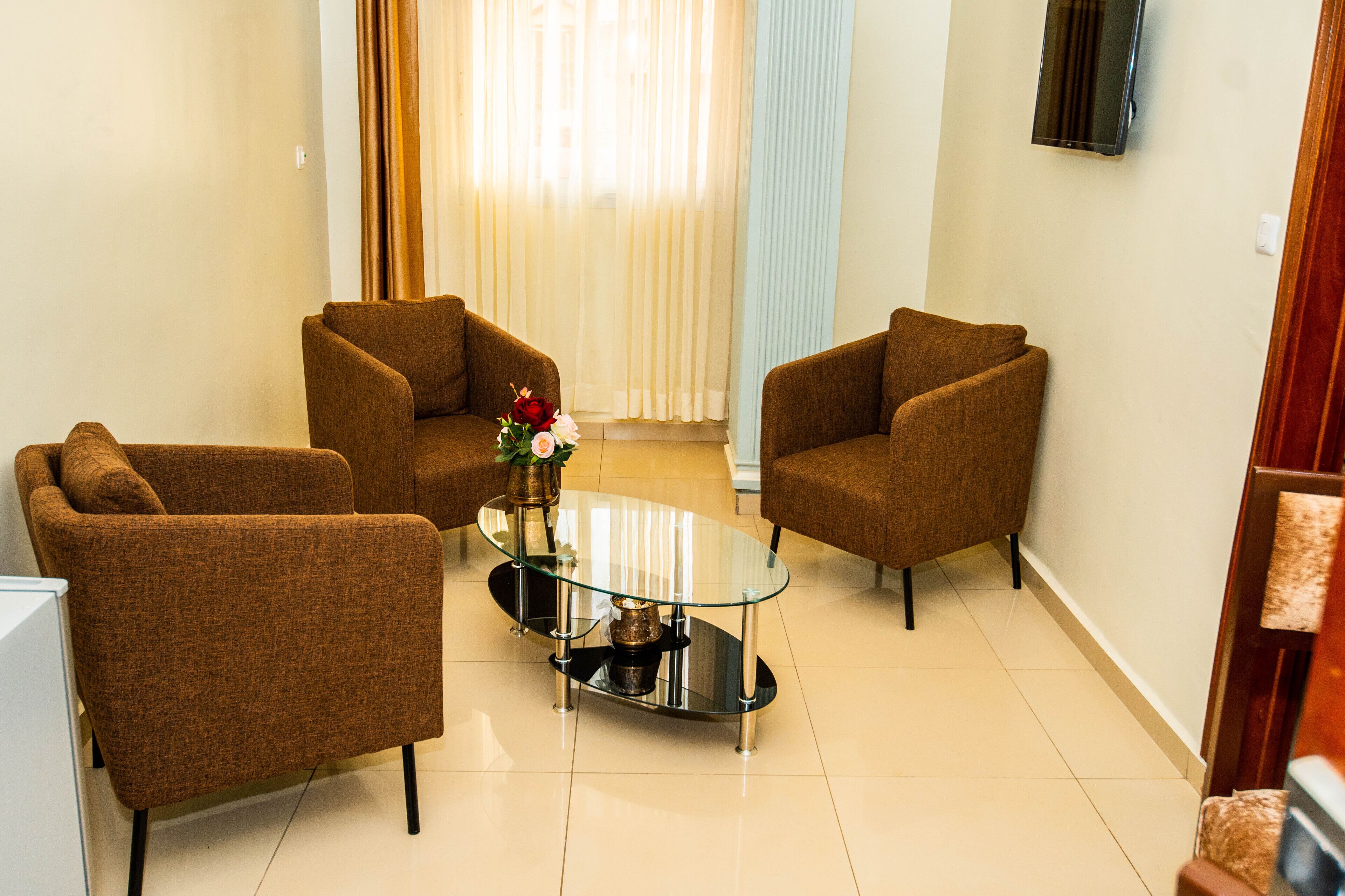 A living room with three brown armchairs, a glass coffee table, and a vase with flowers.