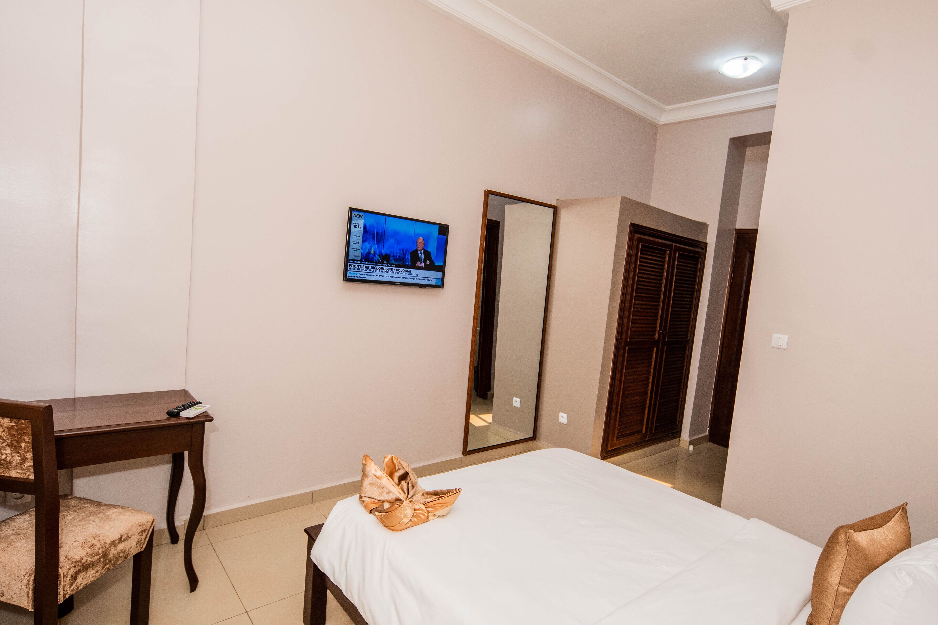 Une chambre d’hôtel comprenant un lit, un bureau avec une chaise, un téléviseur fixé au mur et un miroir.