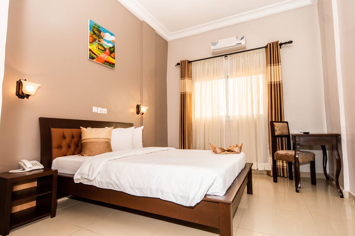 A hotel room with a large bed, bedside lamps, a desk, and a chair.