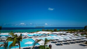 A resort with multiple swimming pools, sun loungers, and umbrellas, overlooking a clear blue sea and a distant island. - The Mora Zanzibar - Luxury All Inclusive (Matemwe)