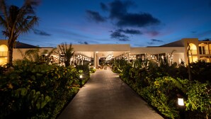 A well-lit pathway leading to a building with multiple balconies and a covered area, surrounded by lush greenery. - The Mora Zanzibar - Luxury All Inclusive (Matemwe)