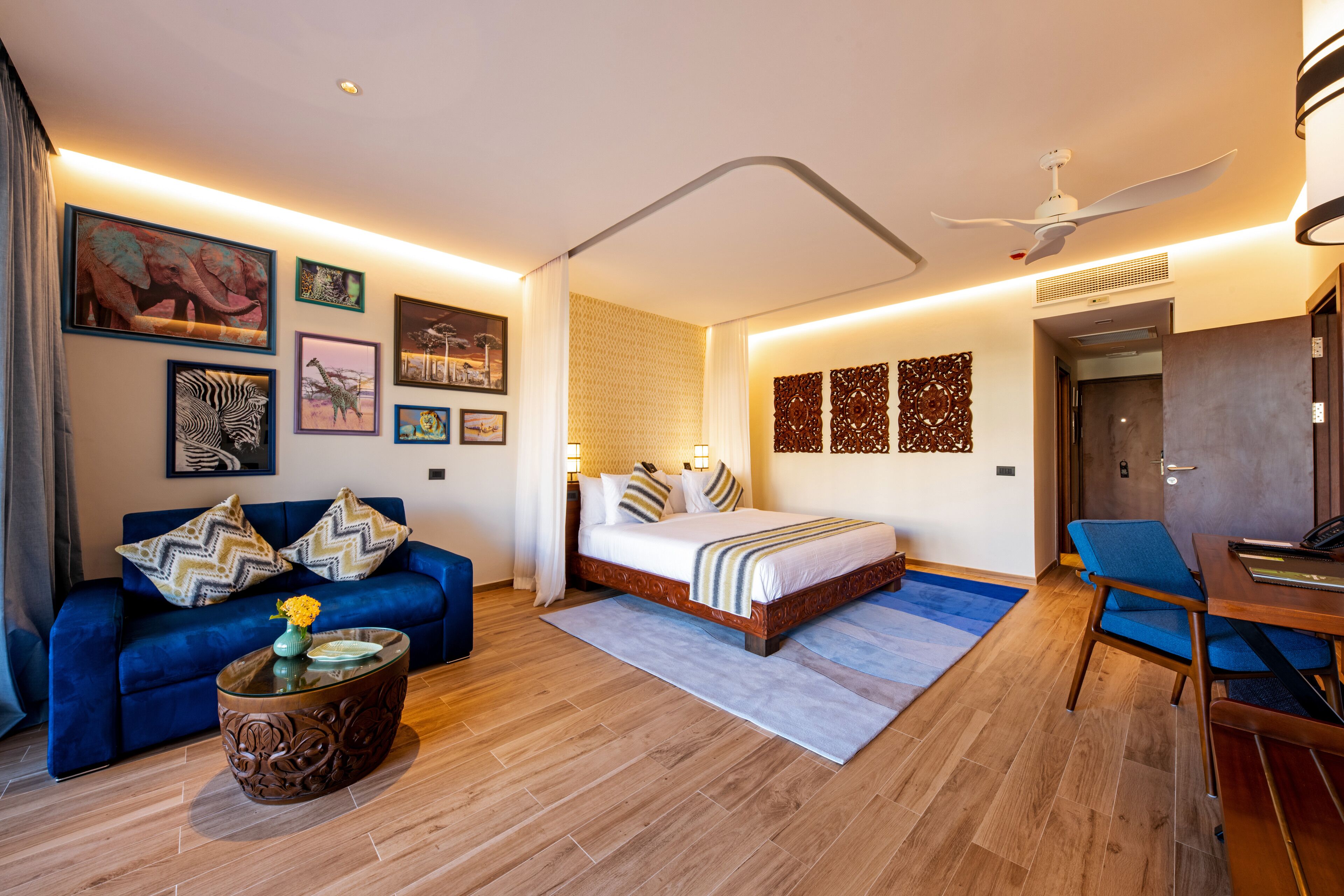 A modern bedroom with a large bed, a blue sofa, a coffee table, and artwork on the walls.