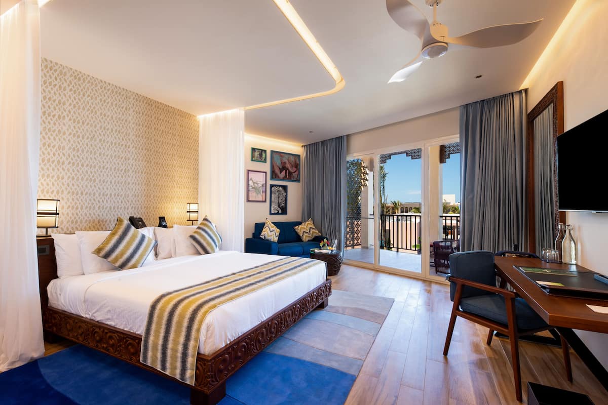 Una habitación de hotel con una cama grande, un escritorio, un televisor y un balcón con cortinas.