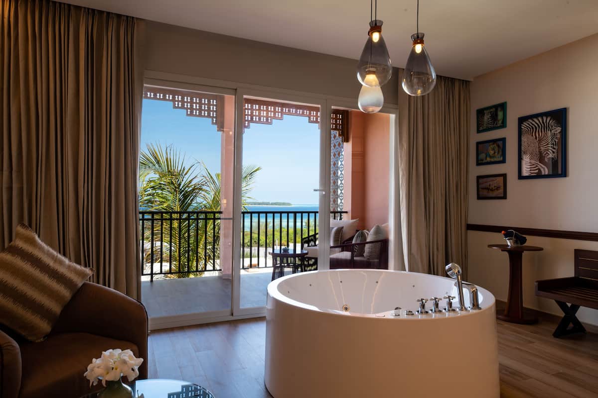Un baño moderno con una bañera independiente, un sofá con un cojín a rayas y vistas al mar a través de grandes puertas correderas.