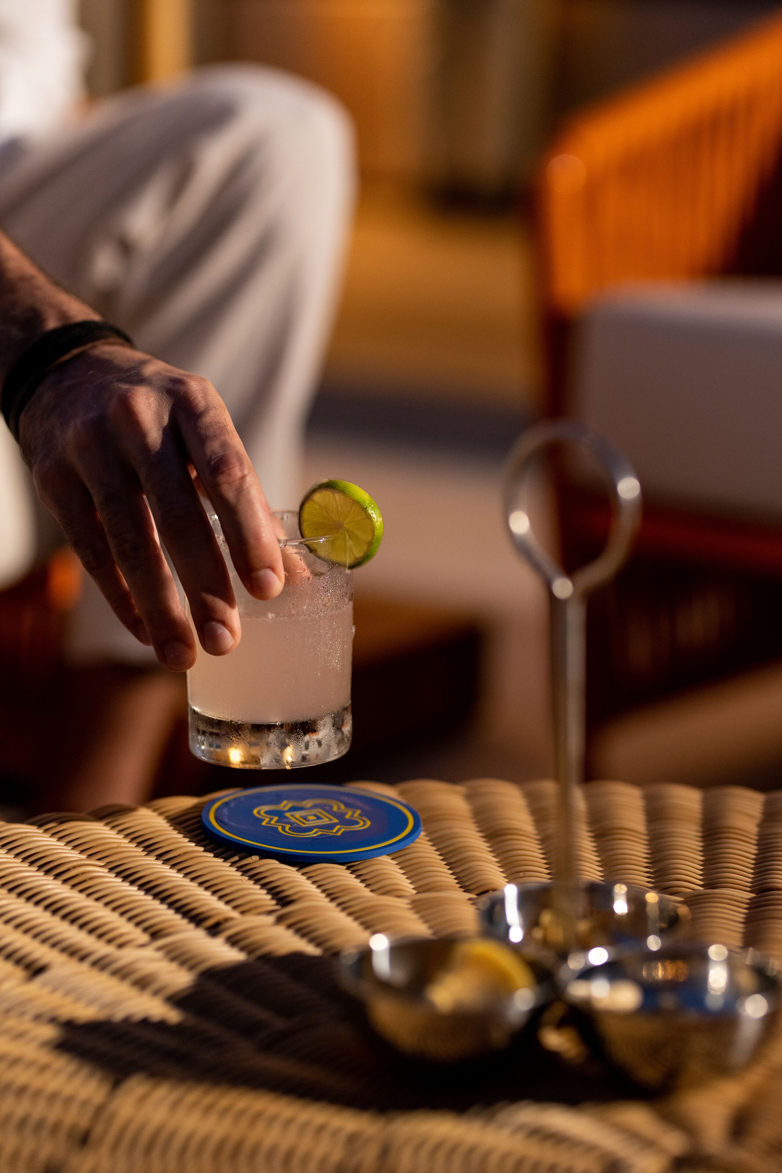 A hand holding a cocktail glass with a lime slice on a coaster.