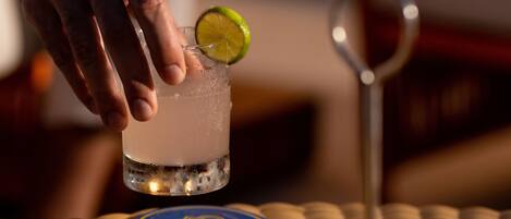 A hand holding a cocktail glass with a lime slice on a coaster.