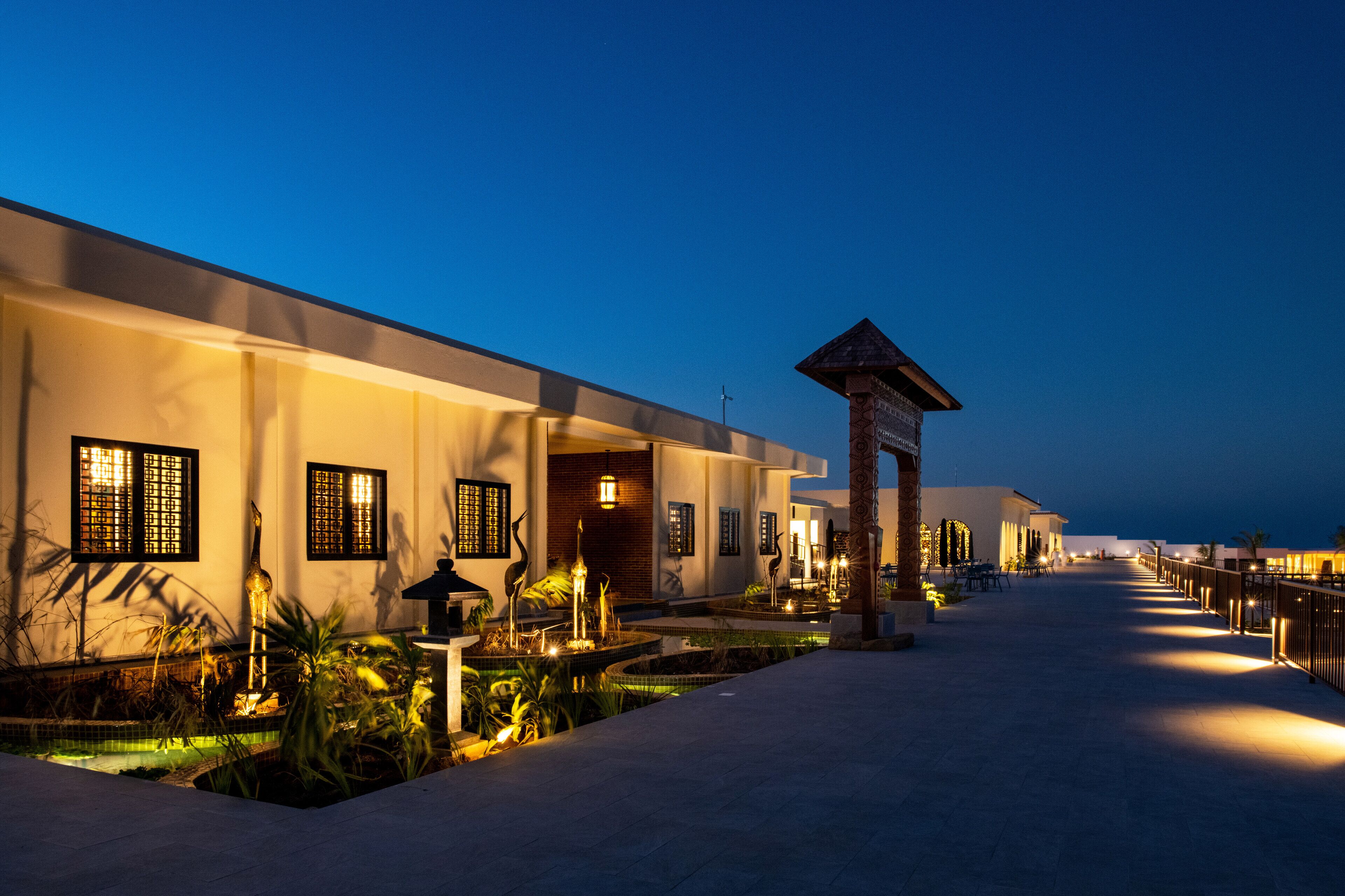 A hotel corridor with a fountain, outdoor seating, and a well-lit pathway.