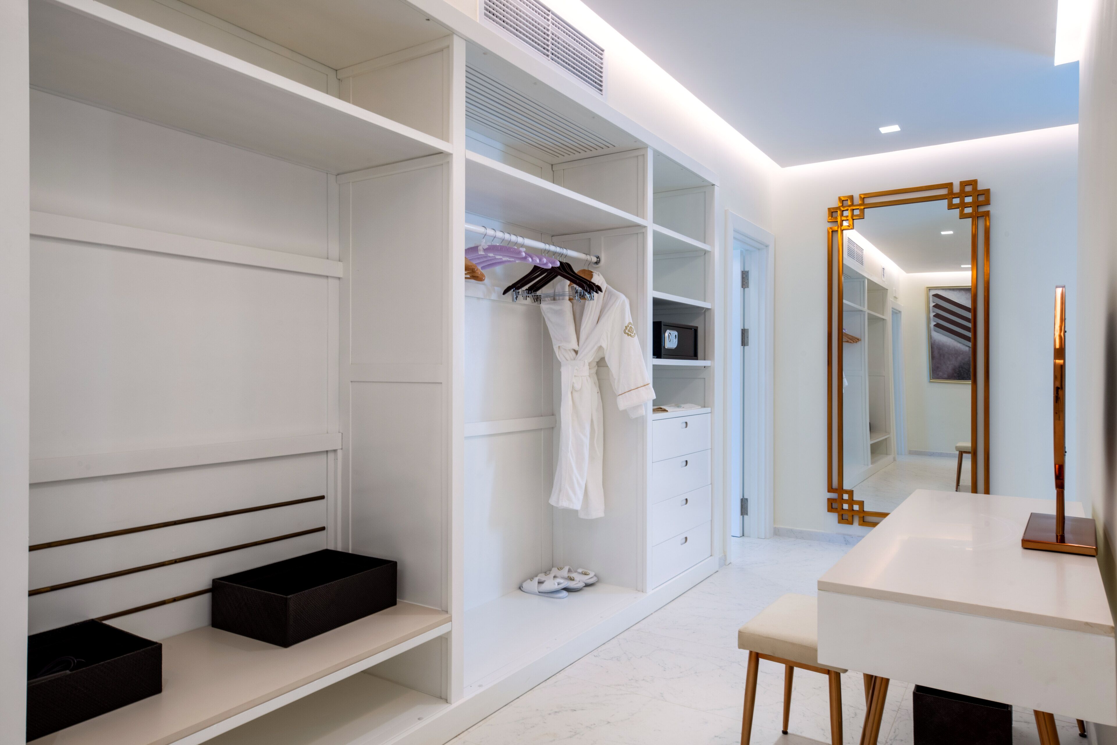 A modern, well-lit walk-in closet with open shelving, a mirror, and a seating area.
