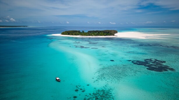 An aerial view of a tropical island with clear turquoise waters, a small boat, and a white sandy beach. - The Mora Zanzibar - Luxury All Inclusive (Matemwe)