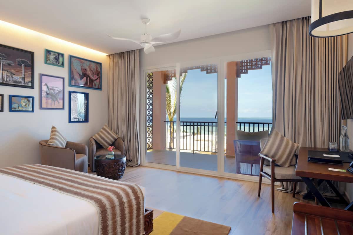 Habitación de hotel con cama, escritorio, silla y balcón con vistas al mar.