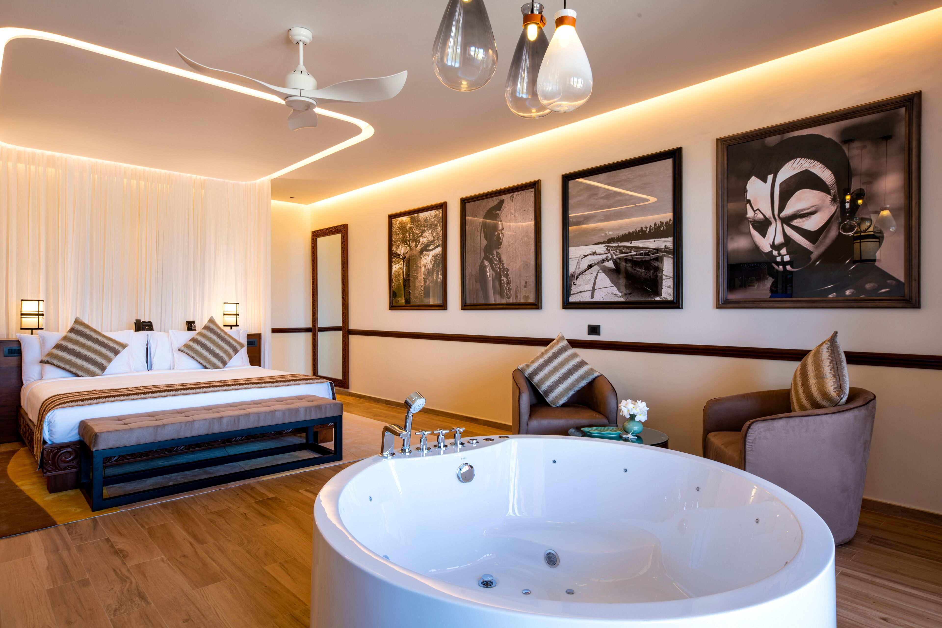 Quarto de hotel moderno com uma cama grande, área de estar com uma poltrona e uma mesa, uma banheira ampla e obras de arte nas paredes.