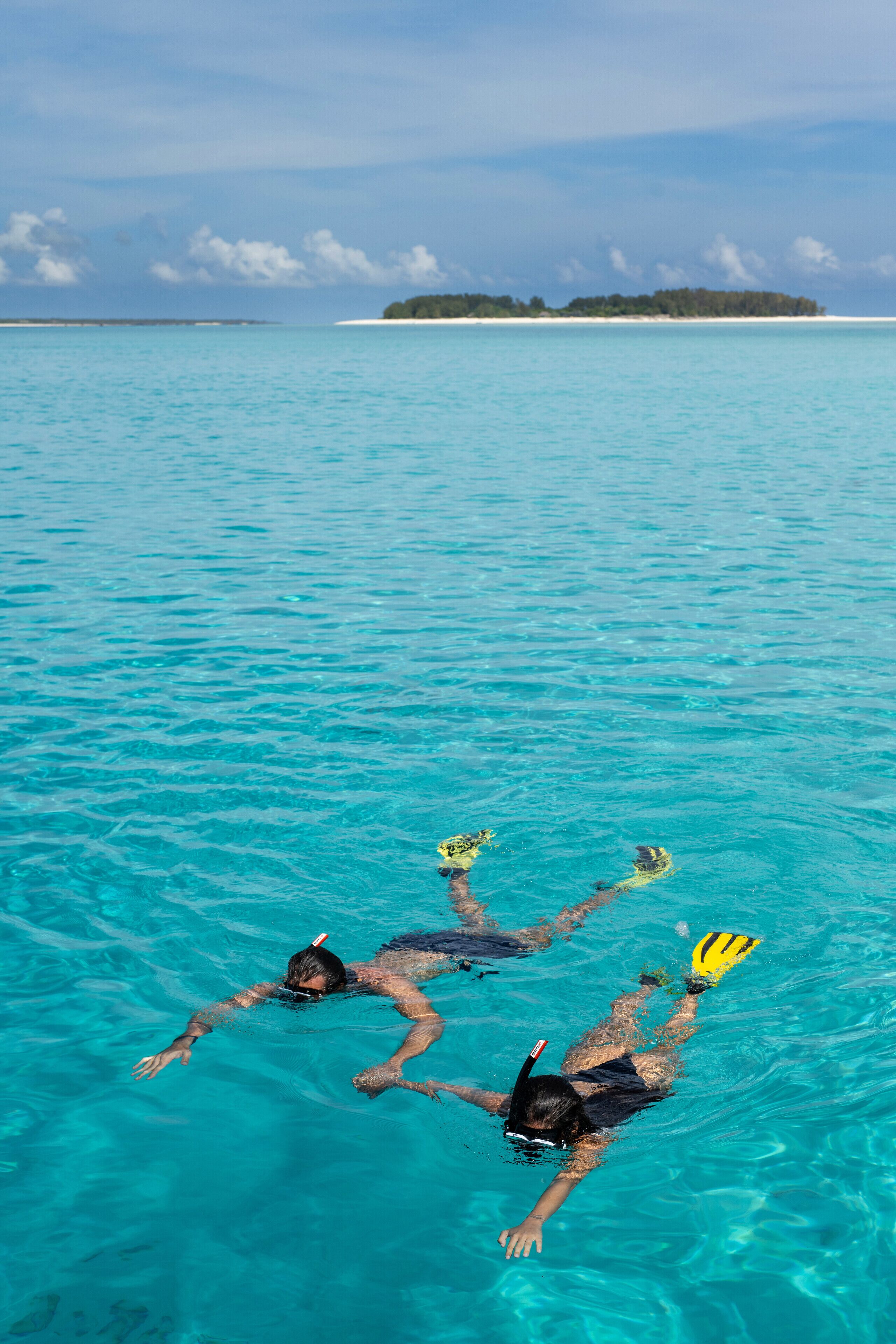 A person swimming in clear turquoise water with a distant island in the background.