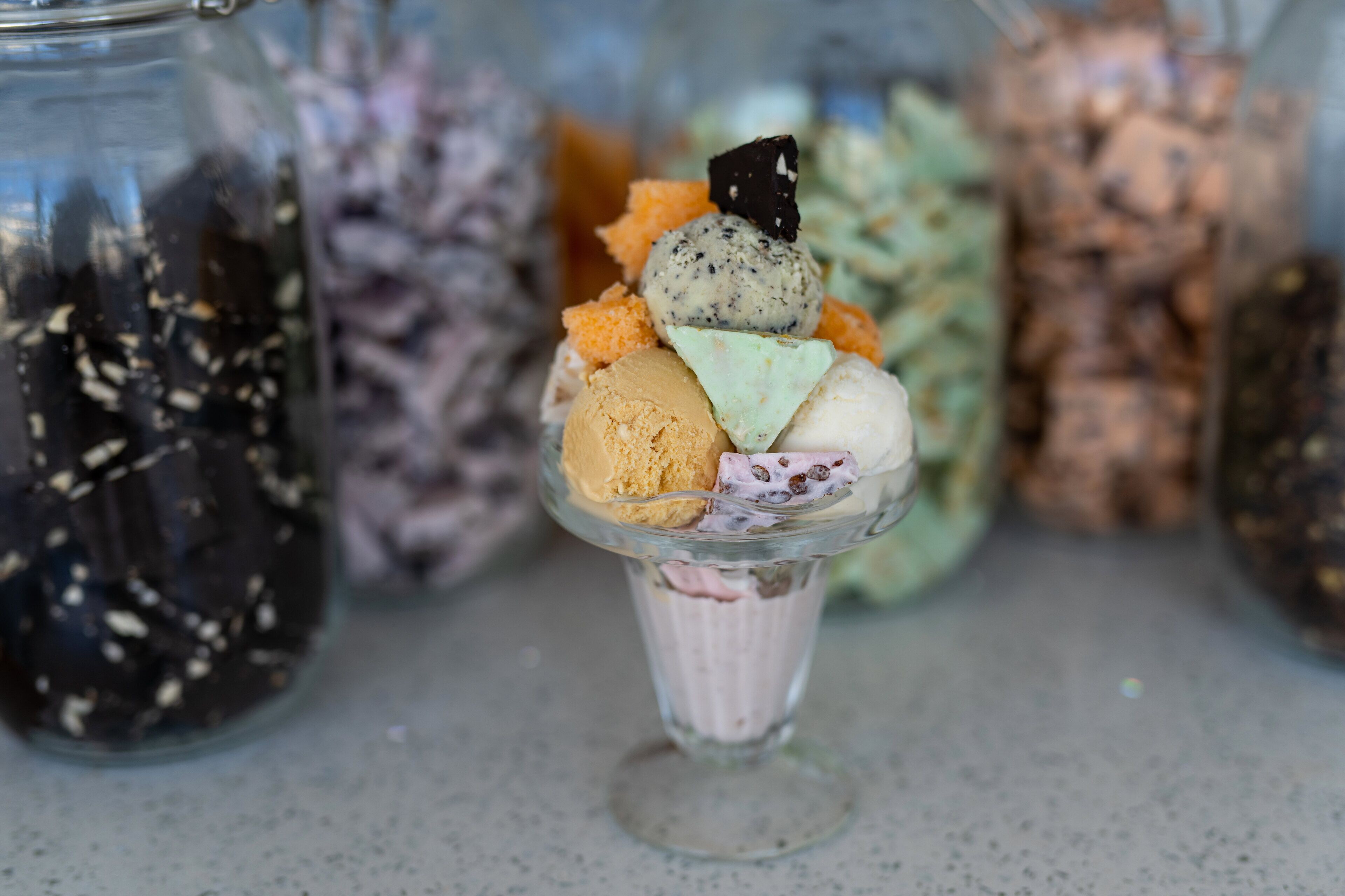 Un postre con distintos sabores de helado y acompañamientos en un recipiente de vidrio.
